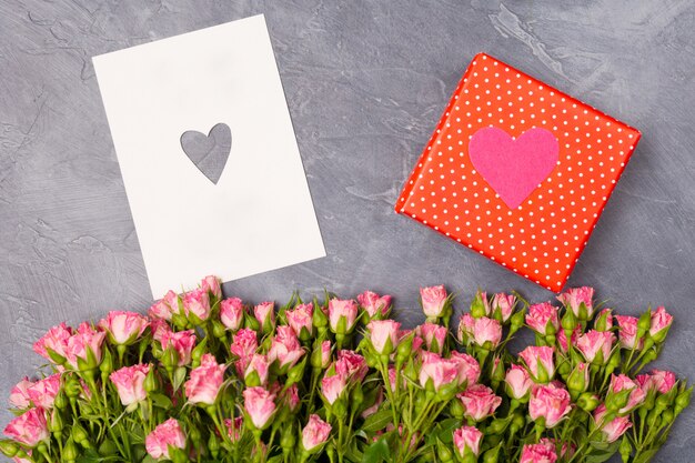 Roze rozen, cadeau in rode doos en kaart met hart op grijze achtergrond Vrouw Valentijnsdag moederdag concept