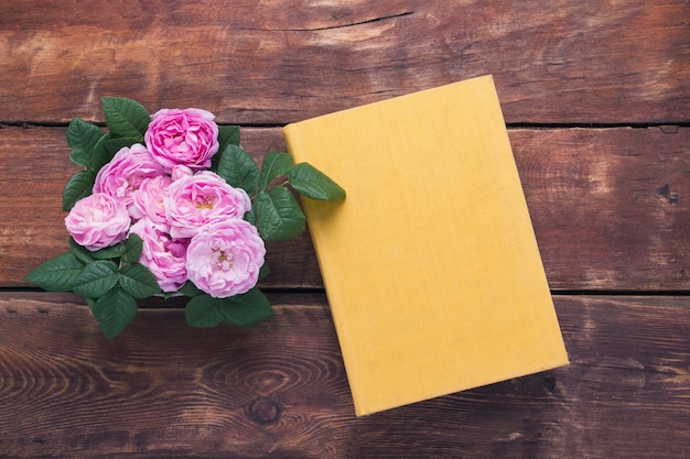 Roze rozen en boek met een gele kaft op een houten achtergrond