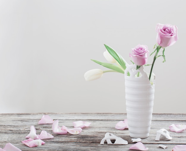 Roze rozen in gebroken vaas op oude houten tafel