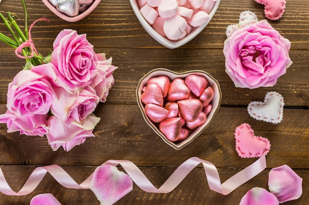 Roze rozen met chocolaatjes op rustieke houten tafel.