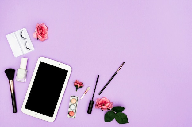 Roze rozen met digitale tablet en make-upborstels op purpere achtergrond