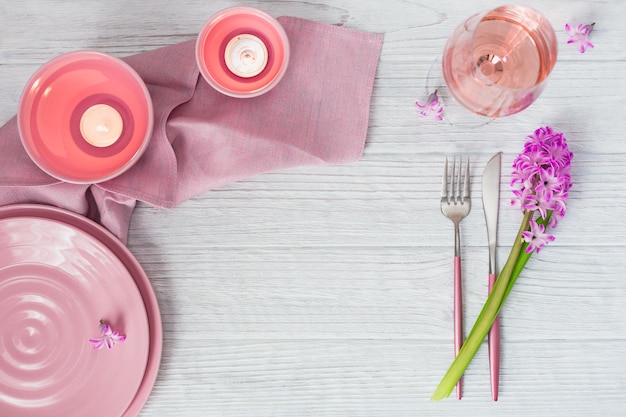 Roze rustieke tafelschikking met paarse hyacinten bloemen linnen servetkaarsen en glas rose wijn op witte houten tafel