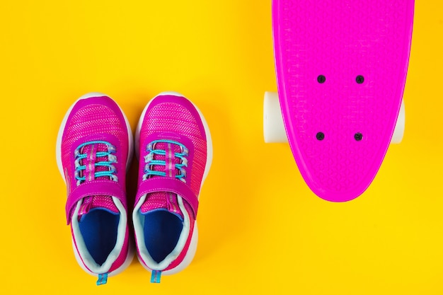 roze skateboard en sneakers op gele achtergrond plat lag