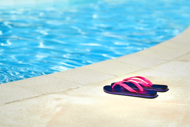 Roze slippers in de buurt van het zwembad met blauw water. Zomer resort. Strandschoenen