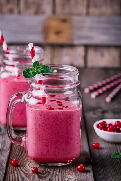 Roze smoothie met wilde veenbessen in metselaarkruik met munt en stro op rustieke houten achtergrond