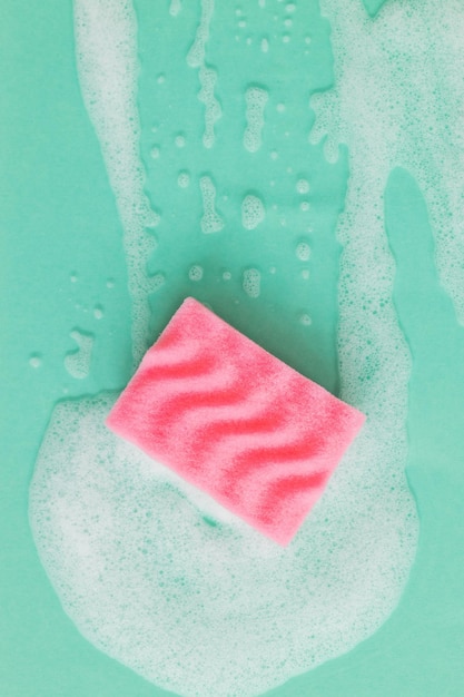 Roze spons met wasmiddelschuim op groene achtergrond close-up Reinigingsconcept