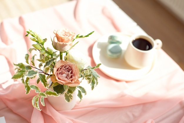 Roze transparant tafelkleed op een houten witte tafel een kopje koffie of thee met Franse bitterkoekjes.