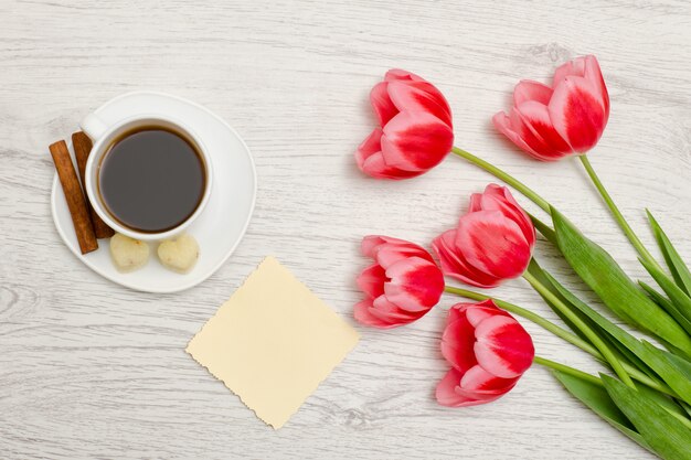 Roze tulpen, blanco vel papier, mok koffie en cinamon, lichte houten achtergrond. bovenaanzicht