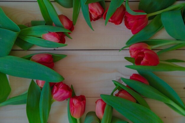 Roze tulpen met groene bladeren liggen in een cirkel met een vrije plek in het midden op een houten achtergrond