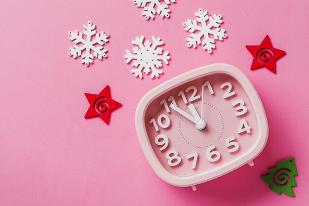 Roze wekker met speelgoed en sneeuwvlokken die op roze oppervlakteachtergrond liggen. Nieuwjaar of Kerstmis concept. Bovenaanzicht. Omgaan met ruimte.