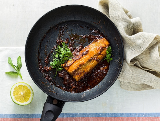 Roze zalmfilet in tomaten-kokossaus in een koekenpan met antiaanbaklaag met peterselie op een tafel met een linnen tafelkleed. gezond familievoedsel