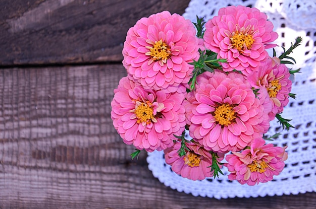 Roze zinnia-bloemen op een houten achtergrond naast een selectieve aandacht voor een servet in vintagestijl