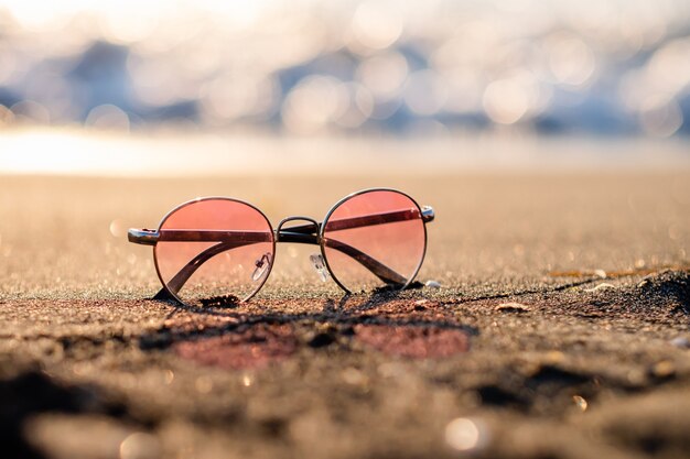 Roze zonnebril liggen op een zandstrand tegen de achtergrond van de zee bij zonsondergang. zomervakantie, ruimte voor tekst