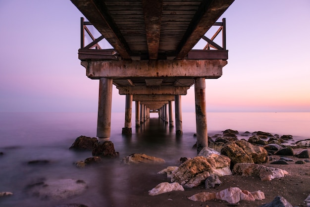 Roze zonsondergang gezien van onderaf een oude houten steiger op een strand aan de Costa del Sol in Marbella.