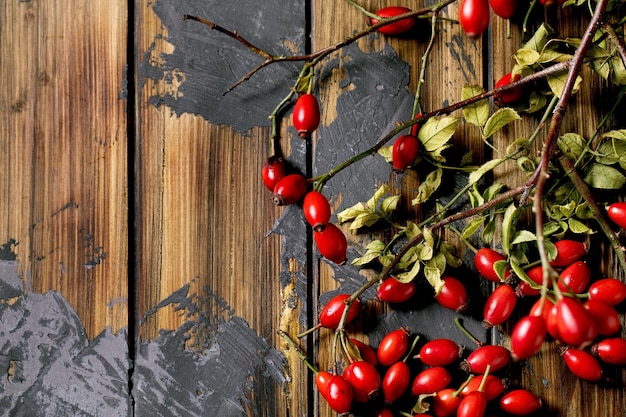 Rozebottelbessen met tak en bladeren op oude houten plankachtergrond. Herfstreserves van vitamines voor de winter. Plat leggen, ruimte kopiëren