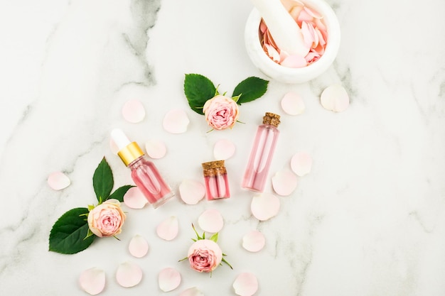 Rozenolie van rozenblaadjes in flessen op een marmeren ondergrond met rozenblaadjes en bloemen. natuurlijke cosmetica.