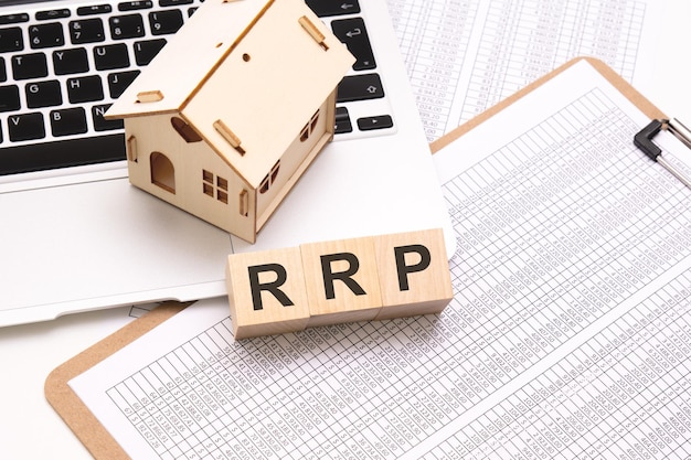 RRP word on wooden cubes on a white background with a table laptop keyboard and a small wooden house