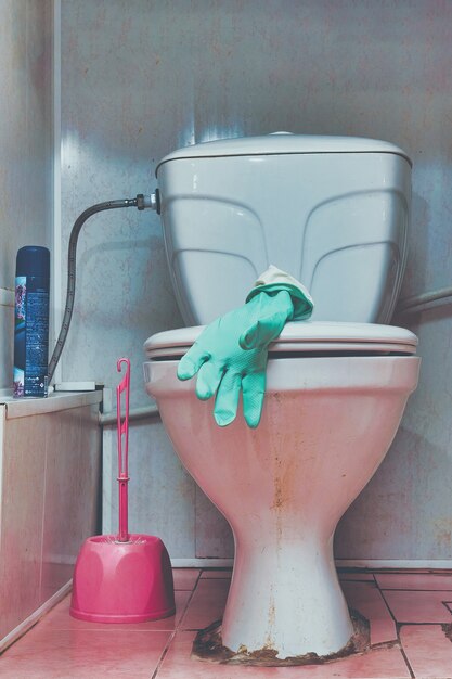 Photo rubber glove on the lid of an old dirty toilet bowl