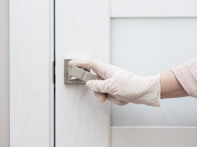 A rubber-gloved hand is holding the door handle of the front door.