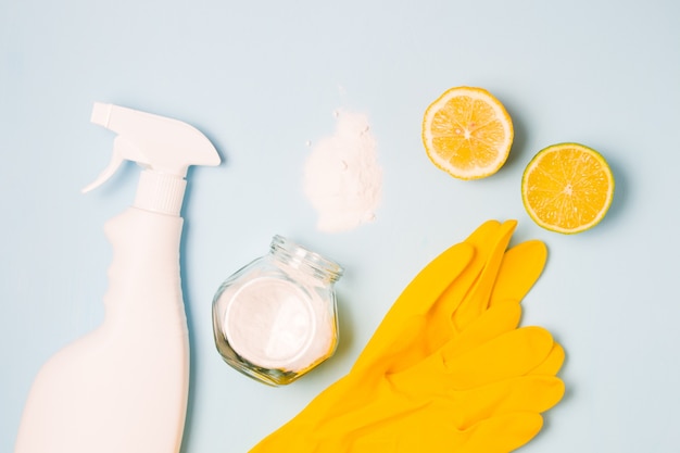 Rubber gloves, a white bottle of spray without a label, half lemon and lime, spilled soda and a glass jar of soda