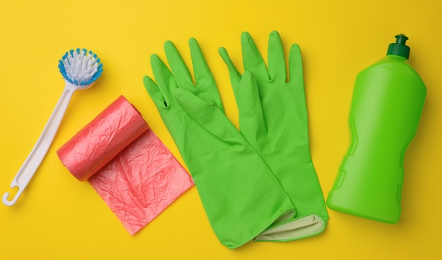 Rubber green gloves for cleaning,Â red trash can plastic bag roll and plastic bottle with detergent on yellow background, set, top view