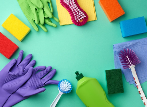 Rubberen handschoenen voor het reinigen, veelkleurige sponzen, borstels en reinigingsvloeistof in een groene plastic fles op een groen oppervlak