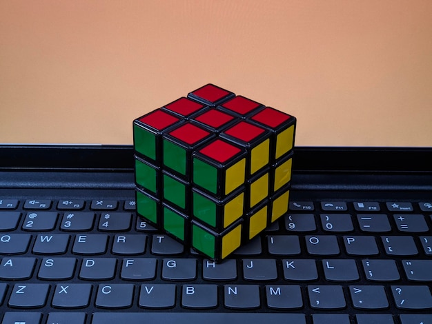 A rubik's cube sits on a keyboard with a orange screen behind it