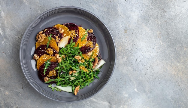 Rucola Bieten- en sinaasappelsalade met walnoten op bord met vorkdressing en kruiden op grijze achtergrond Vitaminesalade Goede voedingsplaats voor tekst bovenaanzicht