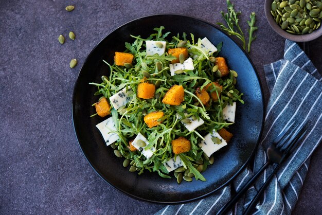 Rucola, blauwe kaas, pompoen, pompoenpitten, salade in een bord, selectieve focus, kopieer ruimte