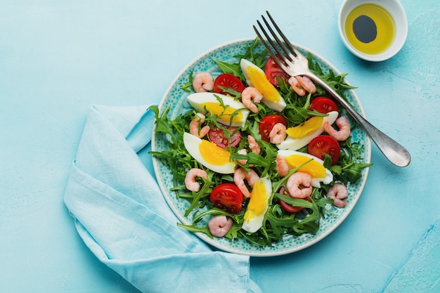 Rucola, komkommer, tomaat, eieren en garnalensalade met sojasaus op keramische plaat. Selectieve aandacht. Bovenaanzicht.