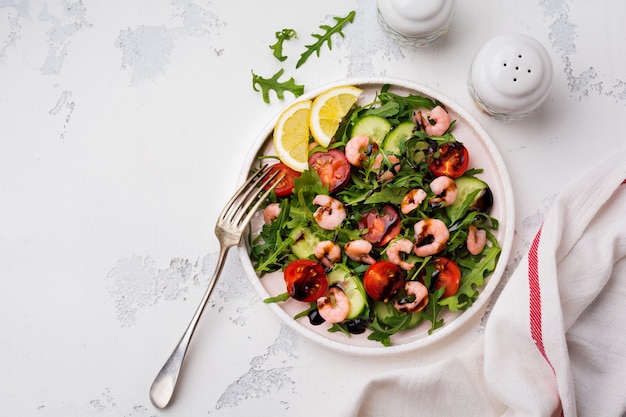 Rucola, komkommer, tomaat en garnalensalade met sojasaus op een keramisch bord