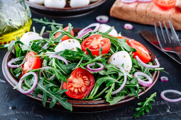 Rucola mozzarella salade met tomaten en rode uien op donkere achtergrond