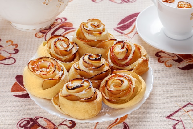 Ruddy baked rolls on a white plate with a cup of fruit apple tea