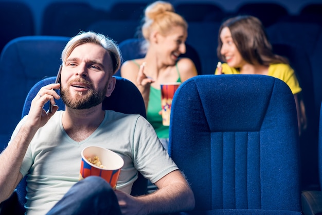 Photo rude man talking with phone disturbing women on the back seats in the cinema