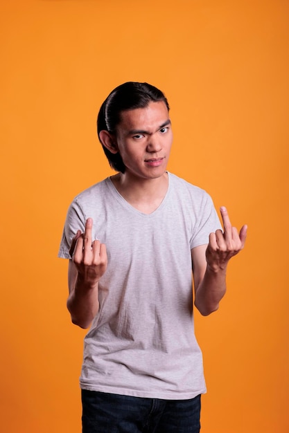 Rude young asian man showing middle fingers, offensive provocative behavior, negative emotions. Aggressive irritated teenager with mad facial expression demonstrating bad sign