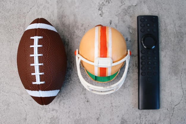 Rugby ball helmet and remote control in watching super bowl games on television concept