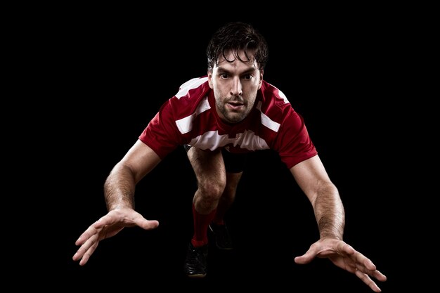 Rugby player in a red uniform giving a tackle. Black wall