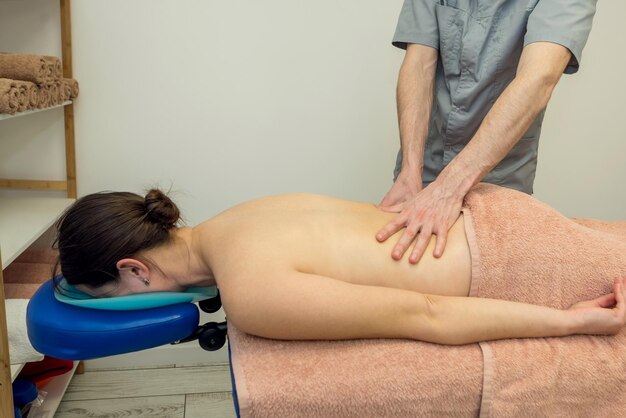 Rugmassage in een massagesalon Lichaamsverzorgingsconcept Een professionele massagetherapeut masseert de rug van een jonge vrouw die op een massagetafel ligt