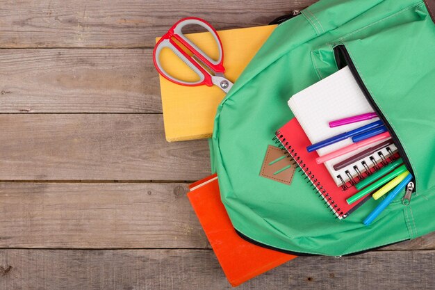 Rugzak en schoolbenodigdheden boeken Kladblok viltstiften schaar op bruin houten tafel