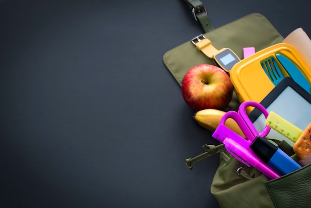 Rugzak met schoolbenodigdheden op zwarte achtergrond.