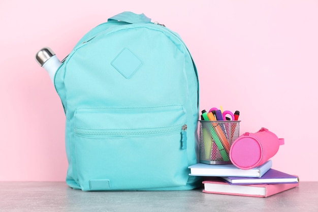 Rugzak met verschillende schoolartikelen op lichtgrijze tafel op roze achtergrond