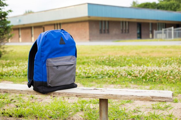 Foto rugzak op een bankje bij de school in het park terug naar school concept