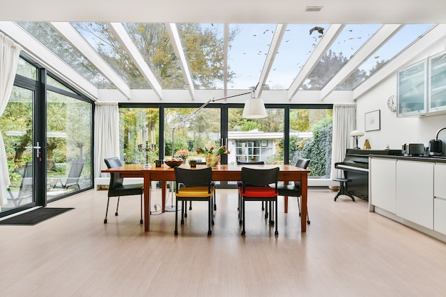 Ruime herenhuiskeuken kamer met glazen wanden en plafond boven houten eettafel bij daglicht