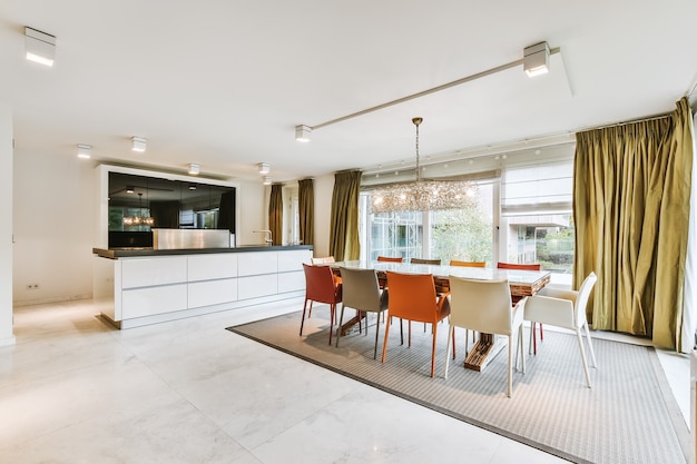 Ruime kamer met open minimalistische keuken en grote eettafel met kleurrijke stoelen onder kroonluchter