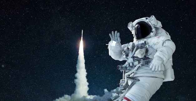 Ruimteman in een ruimtepak en hoed reist in de open ruimte en zwaait met zijn hand tegen de achtergrond van een raketlancering. het ruimteschip stijgt succesvol op. welkom in de ruimte, concept