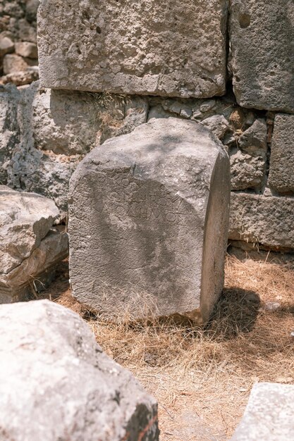 写真 古代言語の碑文のある古い石造りの建物の廃墟の建設は、夏の屋外でトルコの古代リュキアの都市ファセリスの廃墟の古代の発掘調査を探索します