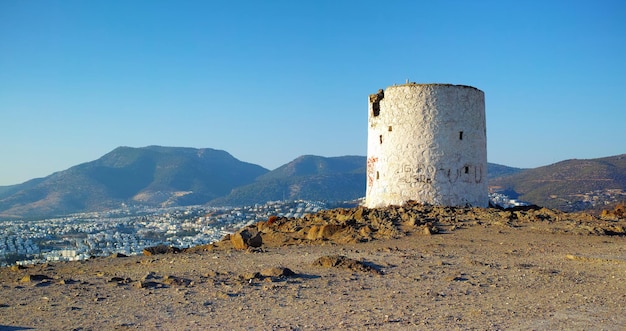 Ruins of broken windmill on a hill overlooking a city\
surrounded by mountains crumbling walls of abandoned lighthouse\
tower a weathered round white stone building architecture of an old\
structure