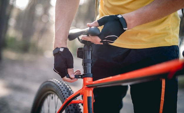 Ruiter die de zithoogte aanpast op een fiets die in het zonnige bos staat