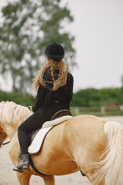 Ruitervrouw die haar paard berijdt op een boerderij. Vrouw heeft lang haar en zwarte kleding. Vrouwelijke ruiter op haar bruin paard.