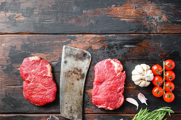 Rump steak organic meat cut, raw marbled beef steak, with old butcher knife cleaver, and seasonings  On dark wooden rustic table,  top view with space for text.